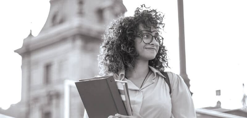 A woman standing in front of a university building holding a notebook