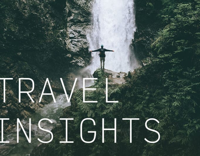 A person at the base of a waterfall with their arms stretched out wide and the caption "Travel Insights".